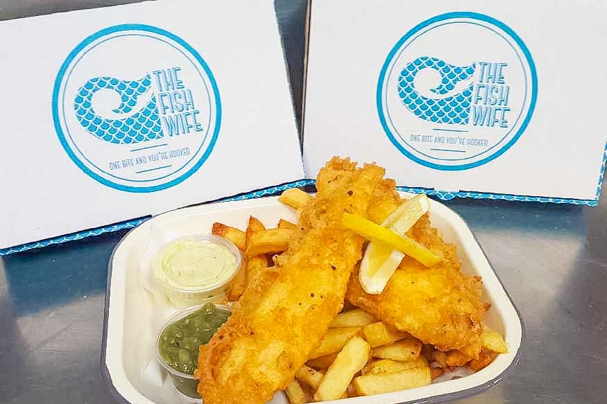 The Fish wife, golden fish fillets and perfectly done chips portion with take away boxes. Two pieces of delicious fish with chips, peas and tartar sauce
