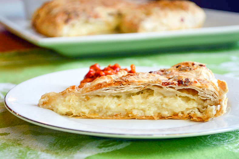 This montenegro food is a flaky pastry with a cheese on a plate sitting on a green table