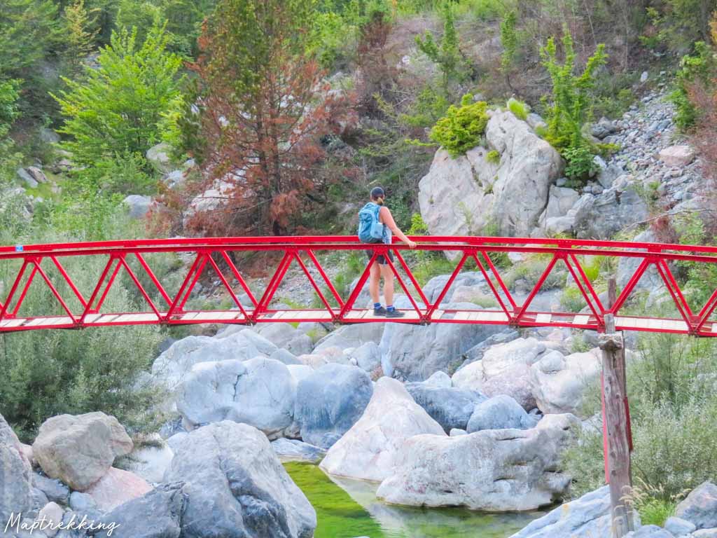 Maria is standing on a red bridge looking into the Albanian wilderness thinking about how traveling is good for the soul