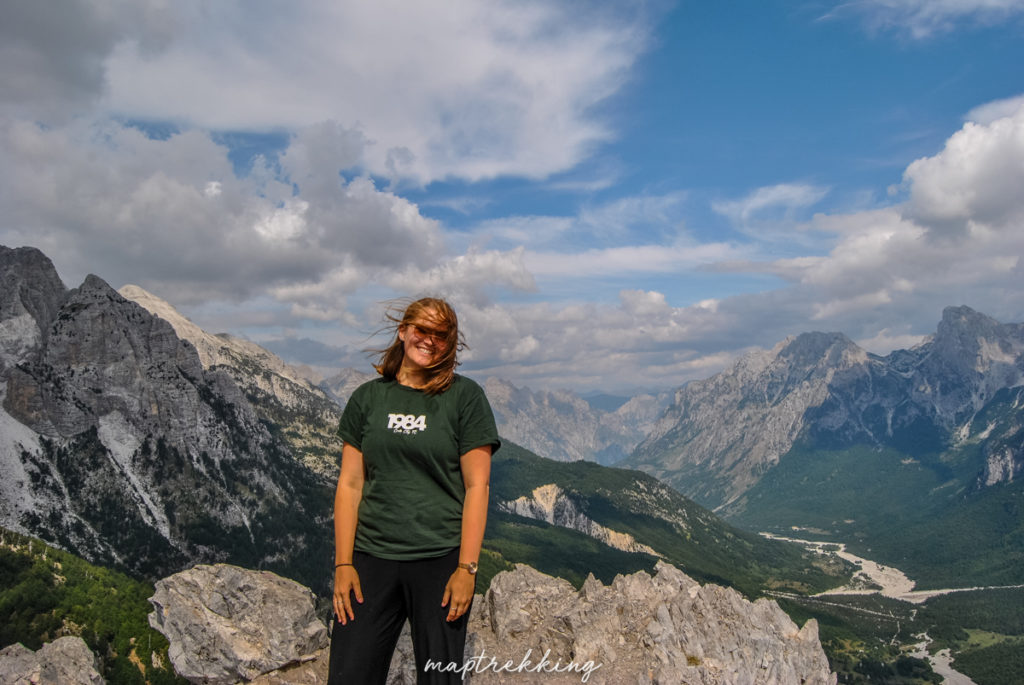 Maria facing the camera with lush green trees lining the accursed Mountains.