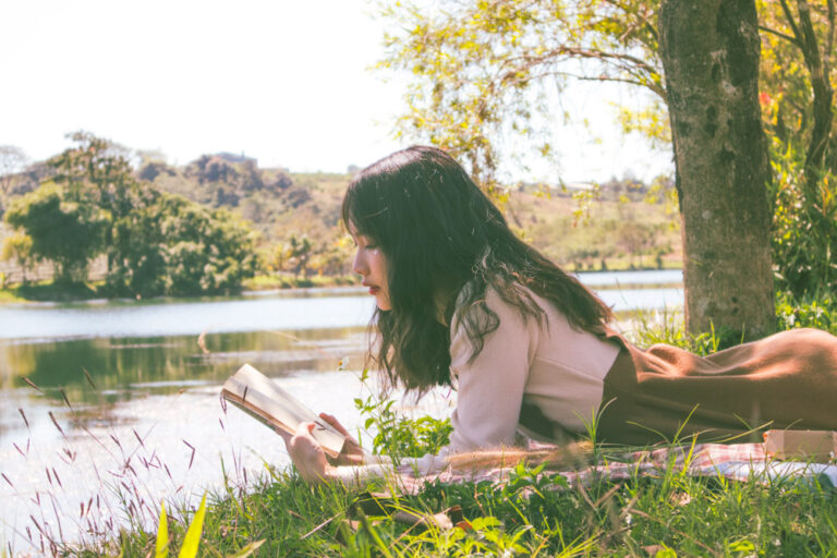a woman reading a slow travel book on the banks of a river