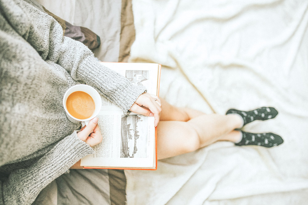 a woman holding a cup of coffee while reading her slow travel book