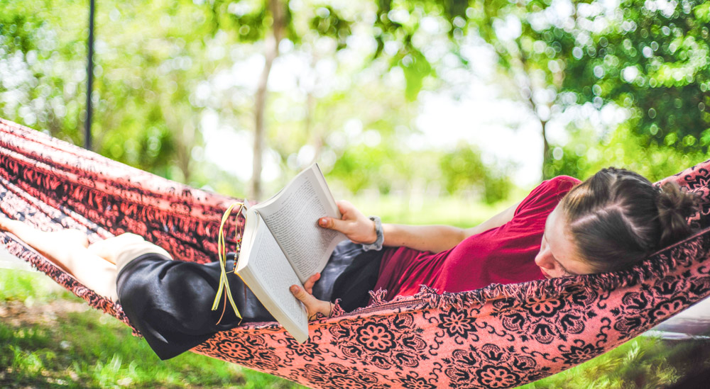 a woman reading a slow travel book while relaxing in a hammock